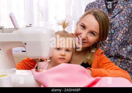 woman is engaged with her daughter interrupting work on a sewing machine Stock Photo