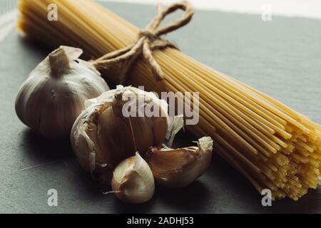 Bulbs and cloves of garlic placed next to spaghetti bunch Stock Photo