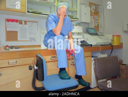 Tired surgeon resting his head on his hand and holding a stethoscope. Stock Photo