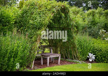 Herbaceous borders and seating area beneath a living Willow structure Stock Photo