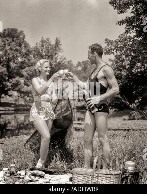 1930s ATHLETIC HEALTHY COUPLE MAN WOMAN WEARING BATHING SUITS TOASTING ONE ANOTHER WHILE ENJOYING OUTDOOR PICNIC BY RURAL LAKE - c3068 HAR001 HARS TEAMWORK ATHLETE PLEASED JOY LIFESTYLE CELEBRATION FEMALES MARRIED RURAL SPOUSE HUSBANDS HEALTHINESS ATHLETICS COPY SPACE FRIENDSHIP FULL-LENGTH LADIES PERSONS CARING MALES ATHLETIC B&W PARTNER FREEDOM HAPPINESS WELLNESS CHEERFUL ADVENTURE LEISURE AND ENJOYING EXTERIOR RECREATION TOASTING SMILES CONNECTION CONCEPTUAL ATHLETES JOYFUL STYLISH BATHING SUITS ONE ANOTHER RELAXATION TOGETHERNESS WHILE WIVES YOUNG ADULT MAN YOUNG ADULT WOMAN Stock Photo