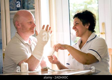 MODEL RELEASED. Treatment after surgery. Nurse applying a bandage to a patient's hand during a home visit. He has had an operation on his hand to corr Stock Photo