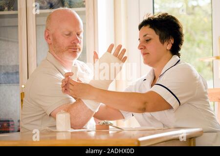 MODEL RELEASED. Treatment after surgery. Nurse applying a bandage to a patient's hand during a home visit. He has had an operation on his hand to corr Stock Photo
