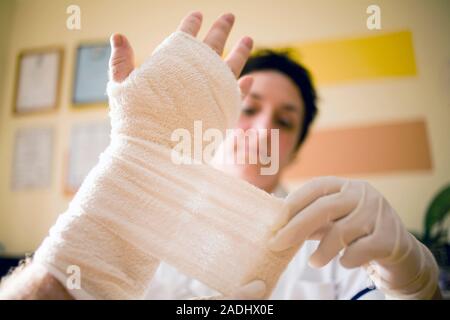 MODEL RELEASED. Treatment after surgery. Treatment after surgery. Nurse applying a bandage to a patient's hand during a home visit. He has had an oper Stock Photo