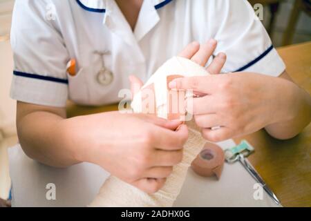 MODEL RELEASED. Treatment after surgery. Nurse applying a bandage to a patient's hand during a home visit. He has had an operation on his hand to corr Stock Photo