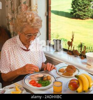 Healthy meal. Elderly woman eating a healthy meal. The meal consists of fish, fruit, vegetables and wholemeal bread. She is squeezing lemon juice onto Stock Photo