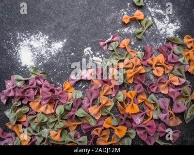 Homemade colorful Italian pasta on grey marble background. Various colors of bow tie tagliatelle, farfalle pasta. Top view. Selecive focus. Stock Photo