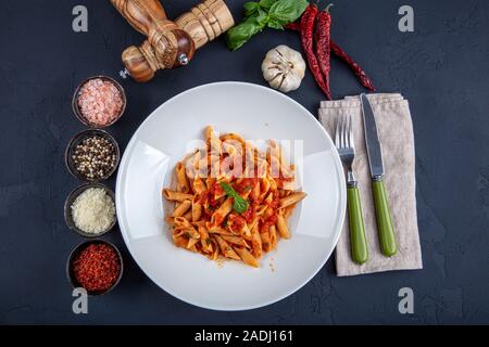 Penne pasta with chili sauce arrabiata. Classic italian penne arrabiata with basil and freshly grated pecorino cheese on a rustic wooden table. Stock Photo