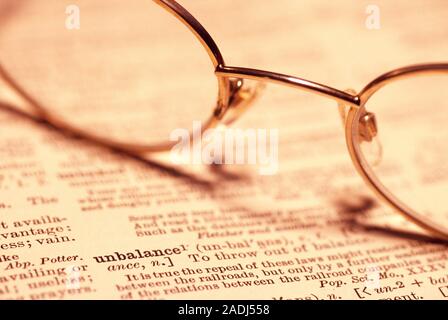 Reading glasses resting on an open dictionary defining the word 'unbalance'. Stock Photo