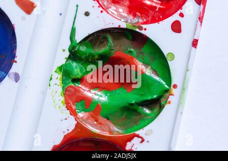 A stain of red paint in a can of green paint. A palette of paints. Modern art. Paint splash. Colorful curl.