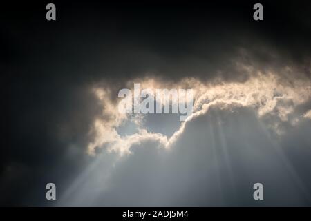 An unusual cloud formation with dark storm clouds meeting light, a bright silver lining as the sun shines through a gap Stock Photo