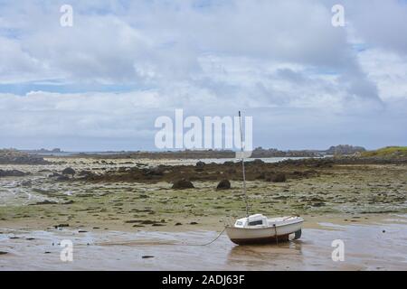 Coast in Brittany at low tide with sand and seaweed and small boats, cloudy blue sky Stock Photo
