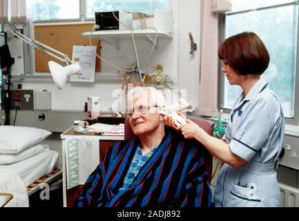 Taking temperature. Hospital nurse using an ear thermometer to take the temperature of a patient. Ear thermometers work by detecting infrared radiatio Stock Photo