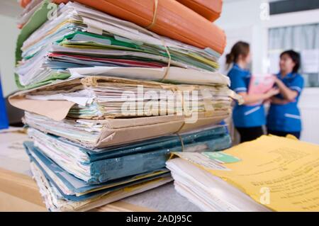 MODEL RELEASED. Medical records. Two nurses in the background are discussing a patient's file. This could represent the difficulties in managing workl Stock Photo