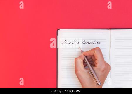 Directly above view of woman's hand writing words New Year Resolution in a notepad on red background Stock Photo