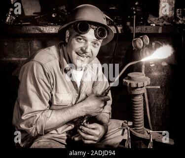 1950s WORKMAN LOOKING AT CAMERA WEARING HARD HAT AND SAFETY GOGGLES PUSHED ONTO FOREHEAD HOLDING AN ACETYLENE WELDING TORCH - s5848 DEB001 HARS SKILLS PROTECTION MUSTACHES HAR POWERFUL LABOR PRIDE WELDER EMPLOYMENT FACIAL HAIR OCCUPATIONS ONTO PUSHED WELDING DEB001 EMPLOYEE MID-ADULT MID-ADULT MAN BLACK AND WHITE CAUCASIAN ETHNICITY LABORING OLD FASHIONED Stock Photo