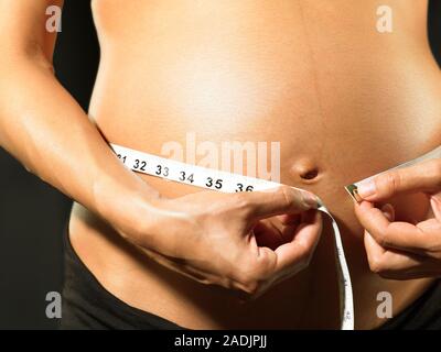 MODEL RELEASED. Pregnant woman measuring her swollen abdomen. She is eight months pregnant. Stock Photo