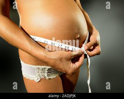 MODEL RELEASED. Pregnant woman measuring her swollen abdomen. She is eight months pregnant. Stock Photo