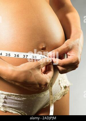 MODEL RELEASED. Pregnant woman measuring her swollen abdomen. She is eight months pregnant. Stock Photo