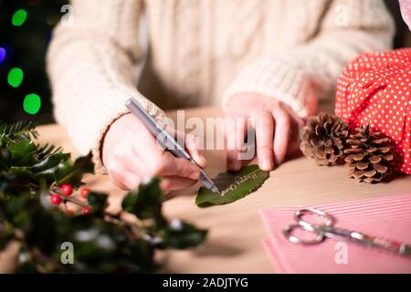 Woman Writing On Gift Tag Made From Bay Leaf For Eco Friendly Christmas Gift Stock Photo