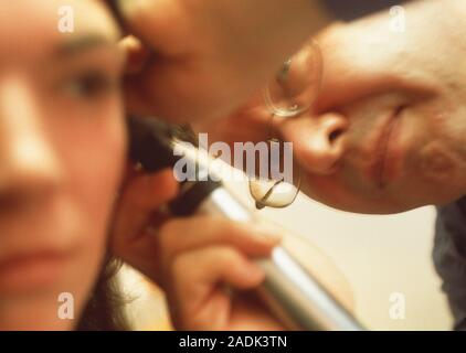 Ear examination. Doctor examining a woman's ear using an otoscope. This device illu- minates the outer ear canal and eardrum, allowing the detection a Stock Photo