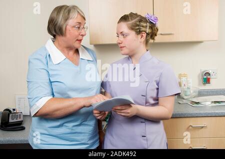 MODEL RELEASED. Health care assistant. General practice nurse (left) discussing a patient's notes with a health care assistant. Health care assistants Stock Photo