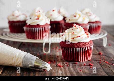 Red velvet cupcakes on a cooling rack and a pipping bag on a rustic wooden table Stock Photo