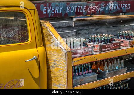 Partial view of an old vintage Coca-Cola delivery truck with coke bottles lined up in a wooden crate stacked on shelves weathered from sitting outdoor Stock Photo