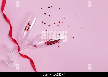 Champagne glasses with red heart shaped confetti and ribbon on pink background. Stock Photo