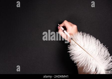Female hand holding feather pen over black background Stock Photo