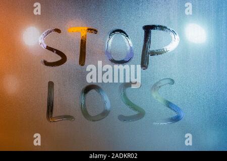 words stop loss written by hand on wet glass at morning with blurry street light background. Stock Photo