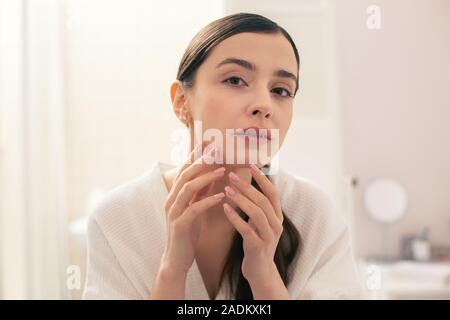 Curious woman analyzing her skin condition and touching her chin Stock Photo
