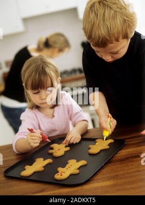 MODEL RELEASED. Making biscuits. Two three year old children decorating freshly baked biscuits with coloured icing. Stock Photo