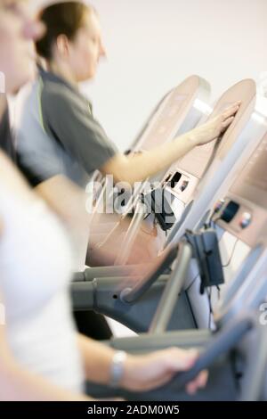 MODEL RELEASED. Running machines. Woman adjusting the controls on a running machine in a gymnasium. The controls on these running machines can be used Stock Photo