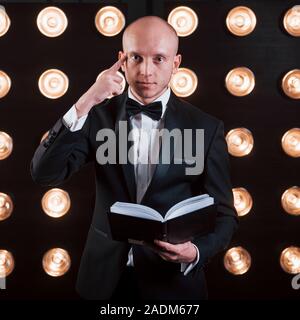 Reading your mind. Magician in black suit standing in the room with special lighting at backstage Stock Photo