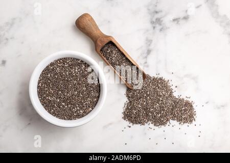 Chia seeds in wooden scoop and bowl on marble table. Salvia hispanica. Copy space, top view Stock Photo