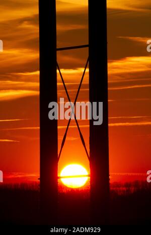 Sunset. The setting Sun is seen behind a set of electrical power lines. The Sun, ultimately, is the source of energy for nearly all the Earth's source Stock Photo