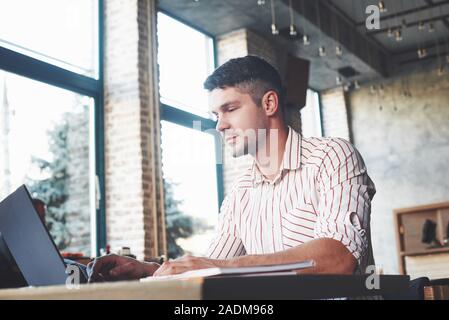 Calm and relaxed. Adult man sits in cafe at daytime and using the laptop for the remote work Stock Photo