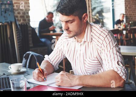 Making some notes. Adult man sits in cafe at daytime and using the laptop for the remote work Stock Photo