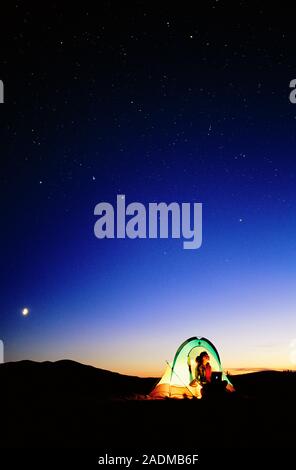 Starry sky and stargazer. Woman sitting in a tent, working at a laptop computer, underneath the starry night sky. The laptop may contain a star chart Stock Photo