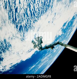An astronaut poses with his arms behind his head while attached by his feet to the space shuttle's remote manipulator arm. The photograph was taken fr Stock Photo