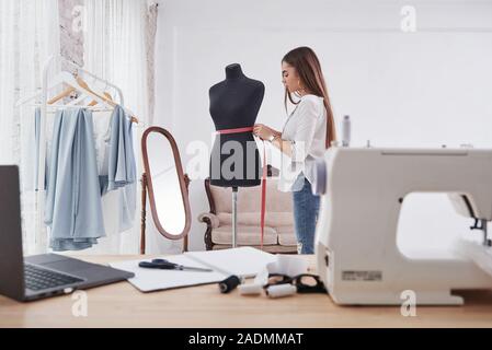 Holding pink measuring tape on the mannequin waist. Female fashion designer works on the new clothes in the workshop Stock Photo