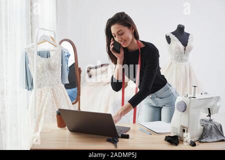 Talks by using smartphone. Female fashion designer works on the new clothes in the workshop Stock Photo