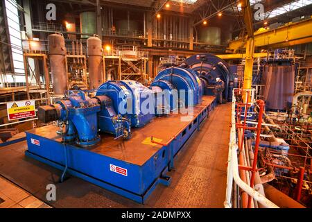 Power station turbine hall. Generator (background) and its exciter (foreground, both are blue) in a coal-fired power station. Steam, produced by the h Stock Photo