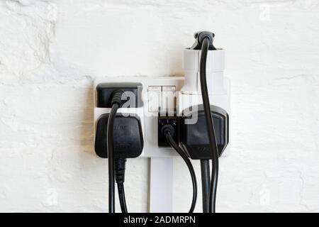 Overloaded electrical power socket. Power sockets containing a plug adaptor and block extension sockets overloaded with plugs. Power sockets are used Stock Photo