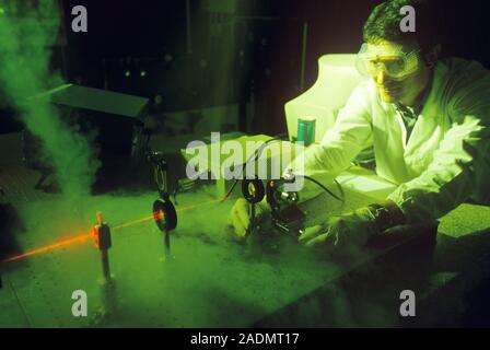 Research laser. Laser (red light) being used in laboratory research. A set of mirrors and lenses are being used to direct the laser. The researcher is Stock Photo
