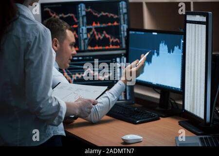 Man shows results. Team of stockbrokers are having a conversation in a office with multiple display screens Stock Photo