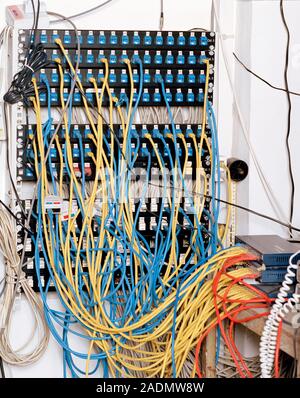 Communications room. Patch panel and wires in an office communications room. The blue and yellow wires carry voice and computer data to and from a net Stock Photo