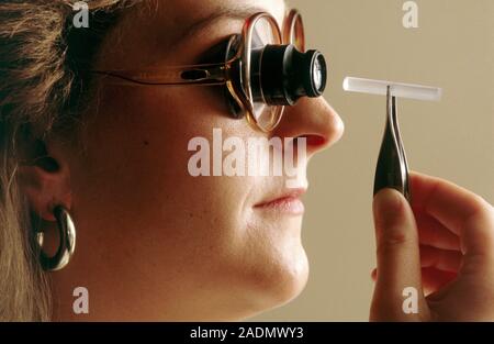 MODEL RELEASED. Fibre optic production. Technician checking the purity of a glass fibre using a magnifying lens. Stock Photo