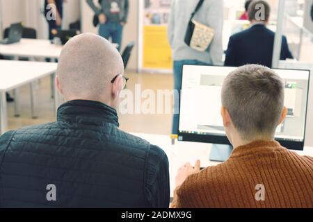 Back view of two male managers or workers look at laptop mock up screen discussing project, colleagues or partners negotiate analyzing statistics and Stock Photo
